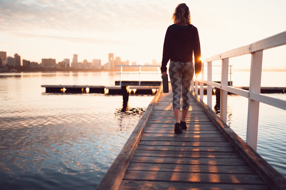 woman standing on dock beside body of water during golden hour