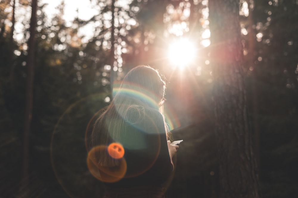 woman using smartphone beside trees during daytime