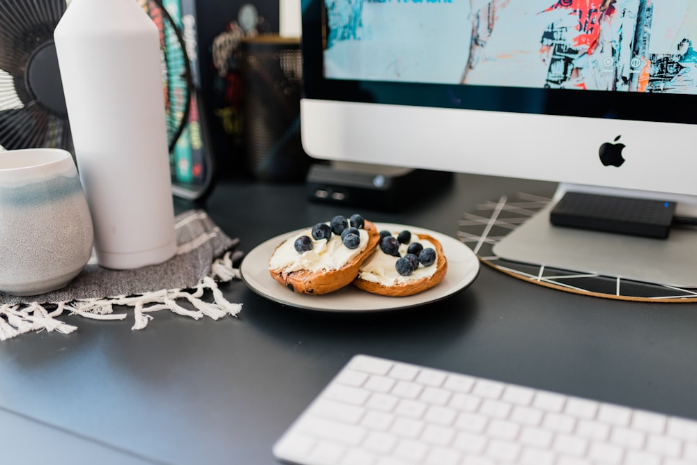 pastries with blueberry toppings on plate beside turned on iMac