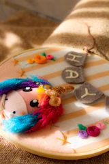 A whimsical unicorn stuffed animal with a colorful mane and sparkly horn resting beside a stack of crochet patterns.