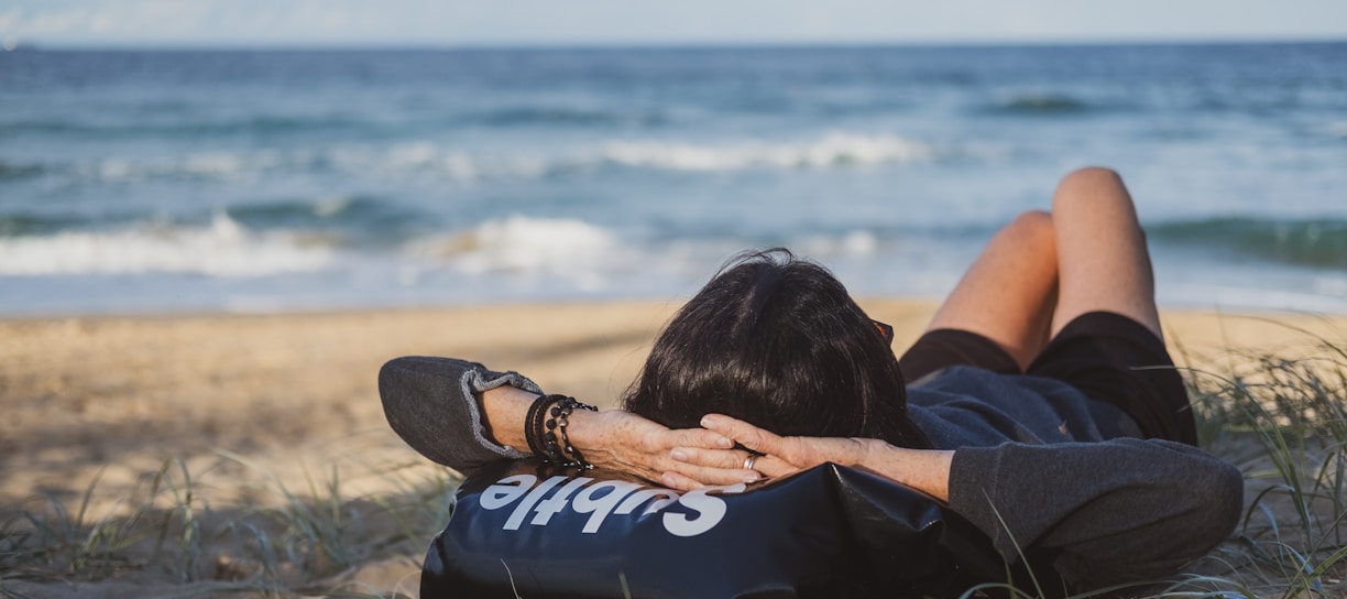 woman lying on grass front of sea at daytime