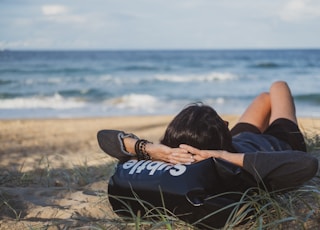 woman lying on grass front of sea at daytime