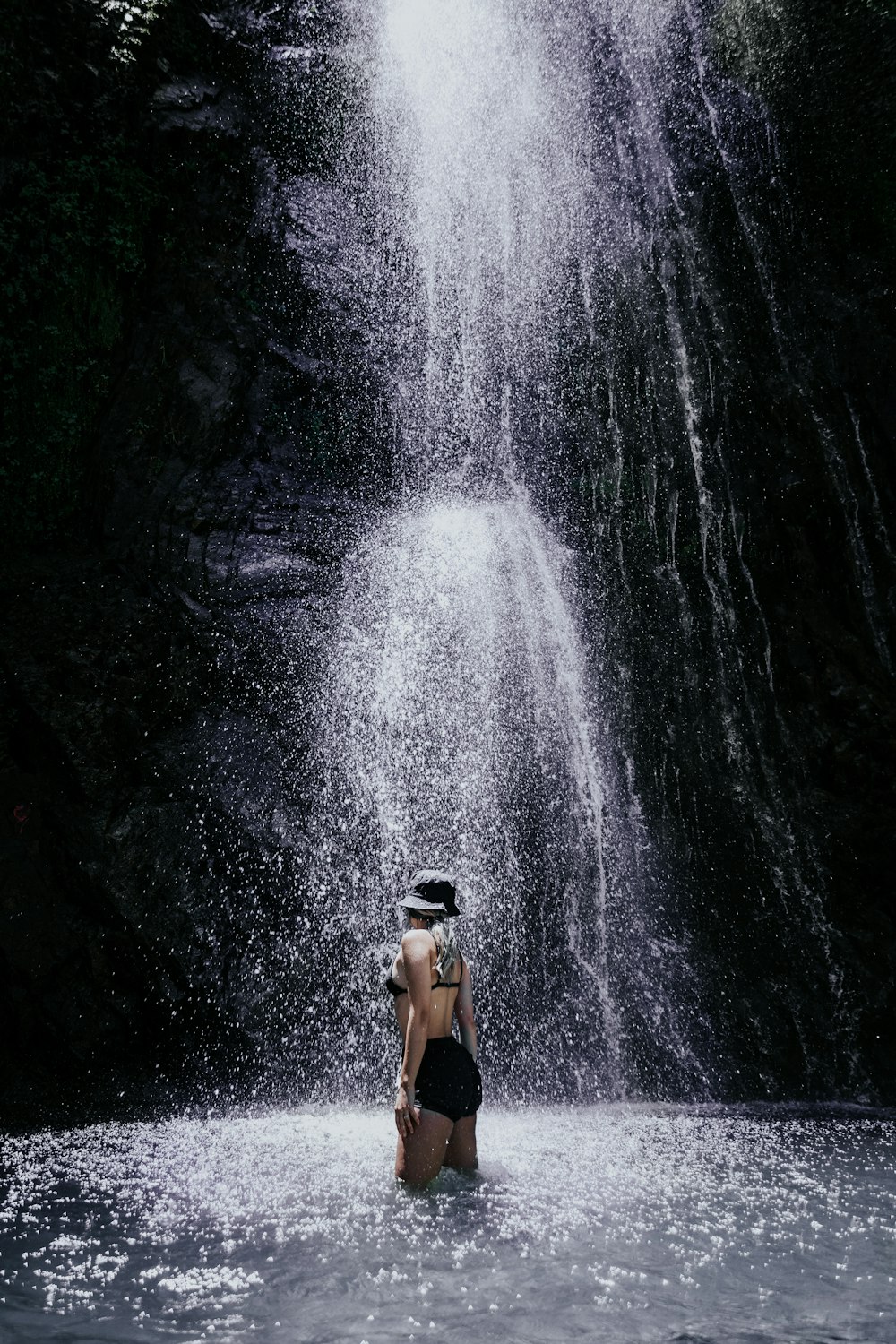 a person standing in a body of water near a waterfall