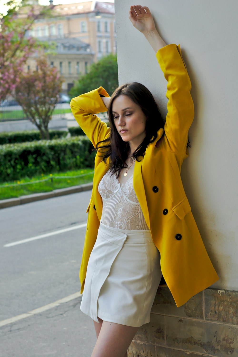 woman in yellow coat leaning on wall