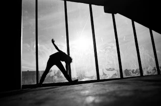 Silhouette of a man stretching by a window in a premium gym, golden light casting shadows.