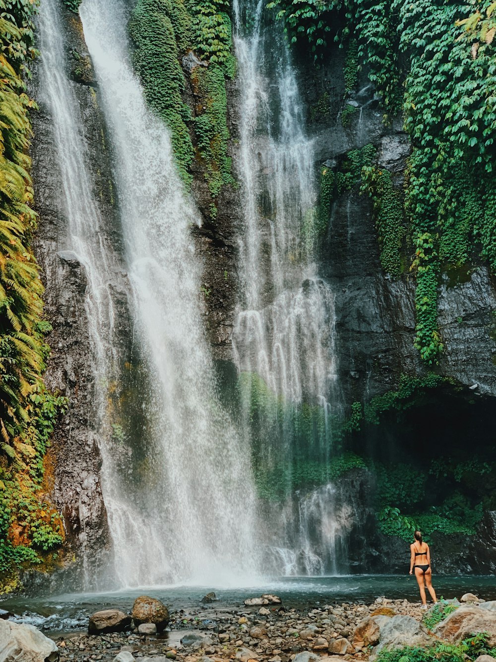 woman wearing blue bikini standing on rock while watching waterfalls