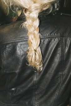 A close-up of a blonde braid resting on the back of a black leather jacket.