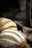 Loaves of freshly baked bread with a rustic crust are displayed on a wooden surface. The bread features a dusting of flour and a pattern of slashes on the top, giving it an artisanal appearance. In the background, there is a dark, blurred setting that enhances the focus on the bread.