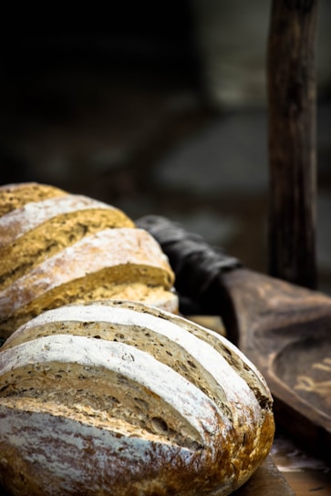 Close-up of a rustic wooden table displaying freshly baked golden crust sourdough loaves dusted with flour.