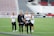A group of women wearing Washington Spirit apparel are on a soccer field, likely preparing for a game or practice. One woman holds a water bottle and they appear to be in a casual and relaxed mood. There are empty seats in the background, suggesting the setting is a stadium.