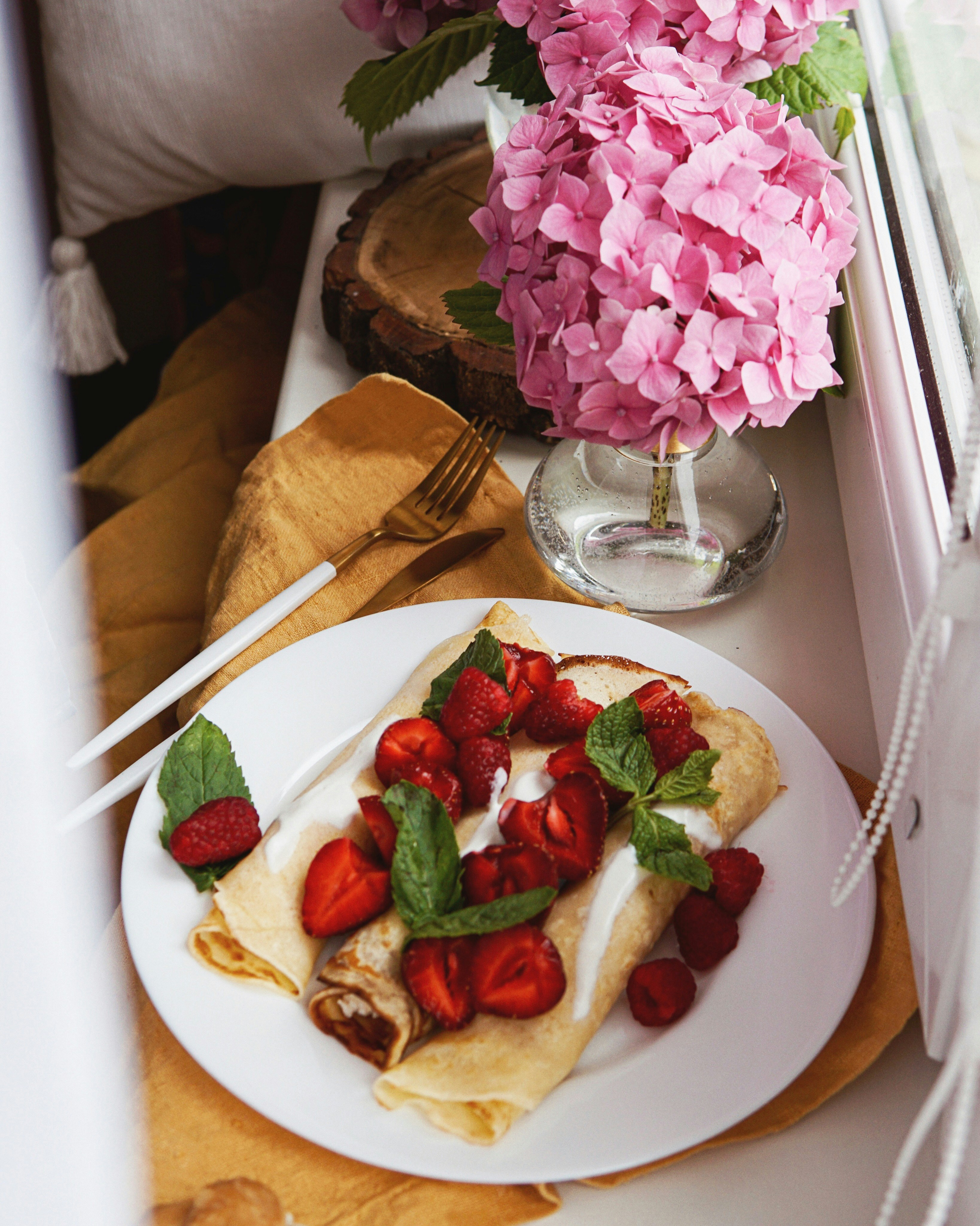 Delicate crepes with colorful fresh berries and honey cream on dark ceramic plate, soft candlelight ambiance