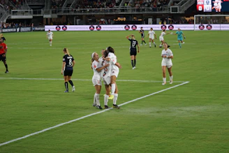 Young female soccer players celebrating a goal on a sunny field.