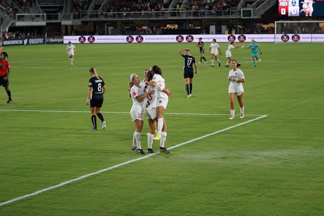 A vibrant women's football match in a sunny Barcelona field with players celebrating a goal.