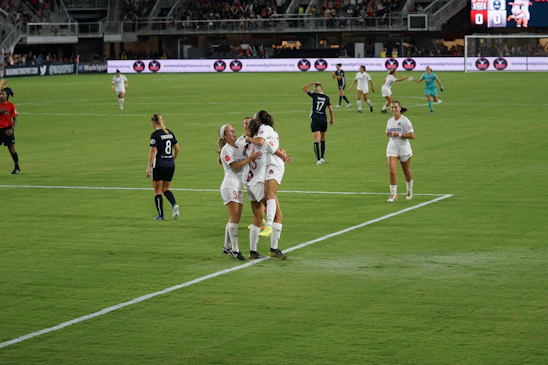 Girls' soccer team celebrating victory on the field with diverse uniforms and joyful expressions.