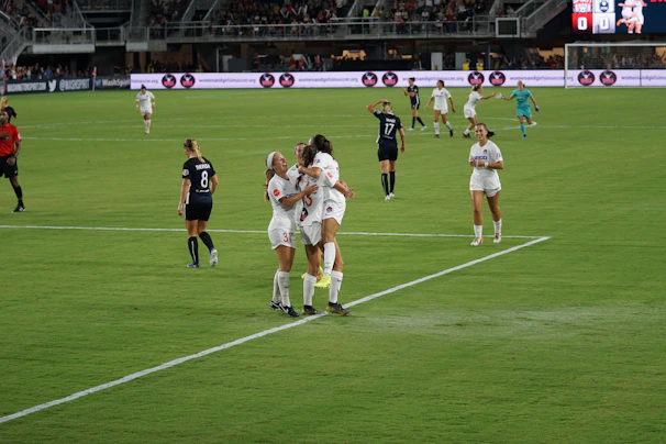Young female soccer players celebrating a goal on a sunny field.