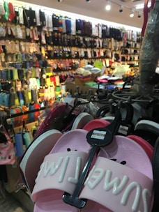 A bustling store with numerous colorful socks and slippers displayed on racks. The foreground features a pair of pink slippers with the inscription 'SMILE' on them, while the background shows rows of hanging socks in various colors and patterns.