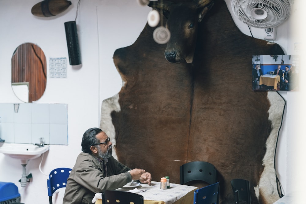 man sitting beside brown cow hide rug on wall