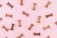 Various dog biscuits in the shape of bones are scattered across a light pink background. The treats are in different shades of brown.