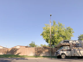 A friendly RV mechanic texting on a smartphone beside a parked RV in a sunny Texas neighborhood.