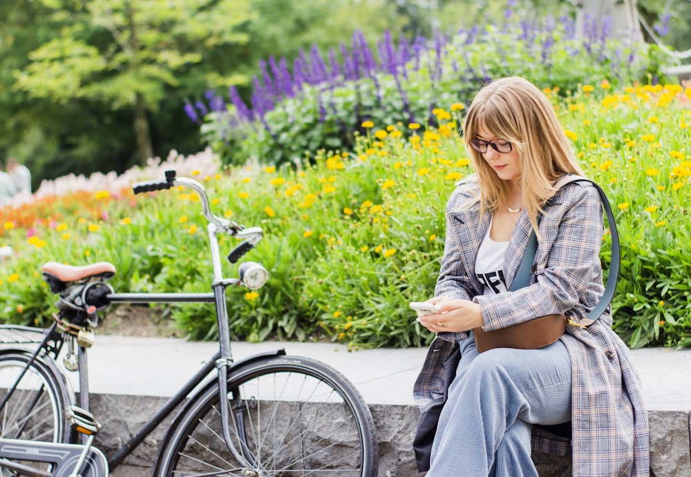 gray bicycle near to woman sitting on wall