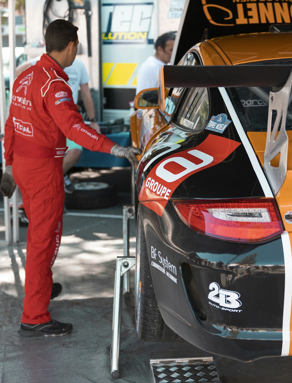 man wearing red and white jacket standing near racing vehicle