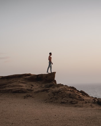 topless man standing on rocky hill