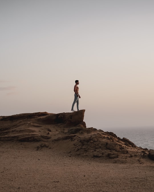 topless man standing on rocky hill in Tamri Morocco