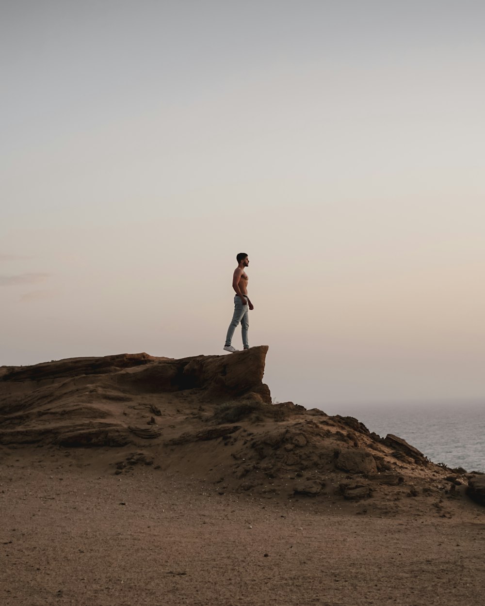 topless man standing on rocky hill