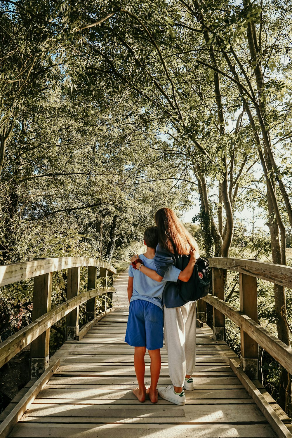 boy and woman standing on wooden bridge