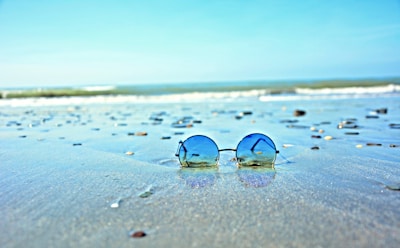 Vintage-style round sunglasses displayed on a sandy beach background with gentle waves
