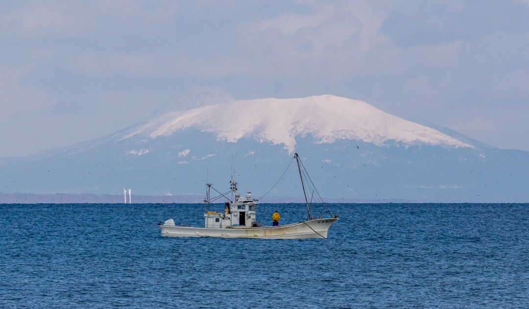 sailing fishing boat overlooking white mountain during daytime