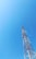 A tall communication tower stands against a clear blue sky. The tower features alternating sections of red and white and is equipped with several antennas.