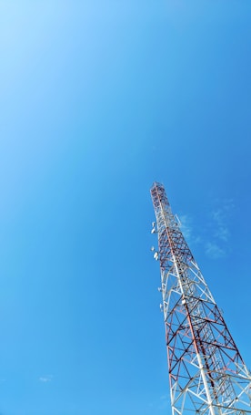 A tall communication tower stands against a clear blue sky. The tower features alternating sections of red and white and is equipped with several antennas.