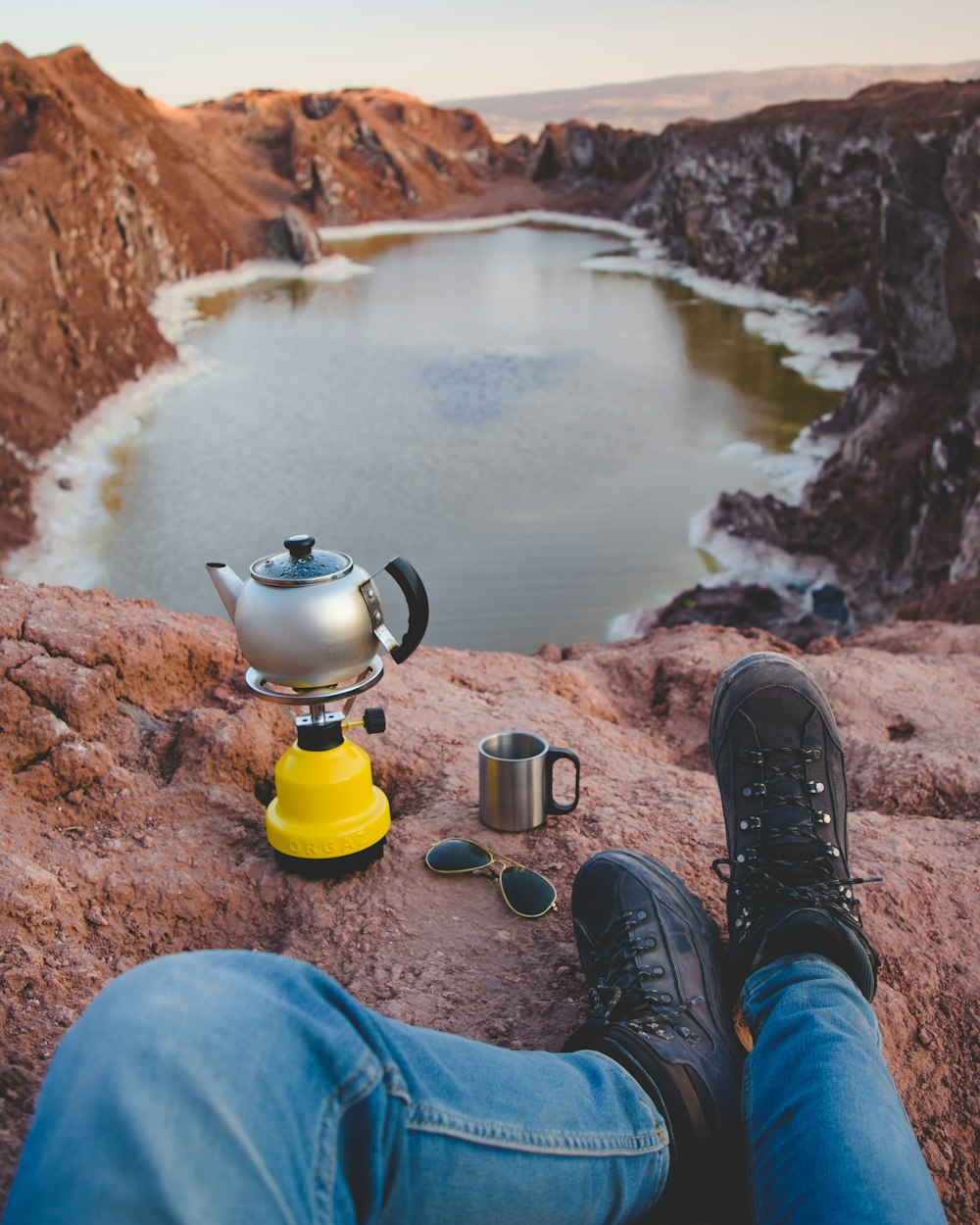 person wearing blue jeans and black boots looking at lake