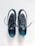 A pair of black sports shoes with white swoosh logos are placed side by side on a clean, light-colored surface. The insoles are blue with a pattern of small black dots, and the laces are neatly tied.