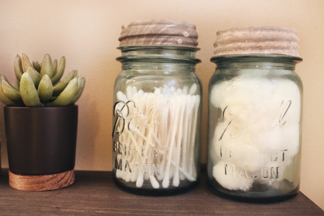 Vintage blue Ball glass jars with zinc lids hold bathroom necessities like q-tips and cotton balls on a stained black shelf which is adorned with a small potted green succulent.