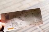 A hand holding an Italian train ticket from Trenitalia. The ticket features detailed text including departure and arrival locations, dates, and a barcode. The background is blurred, focusing attention on the ticket.