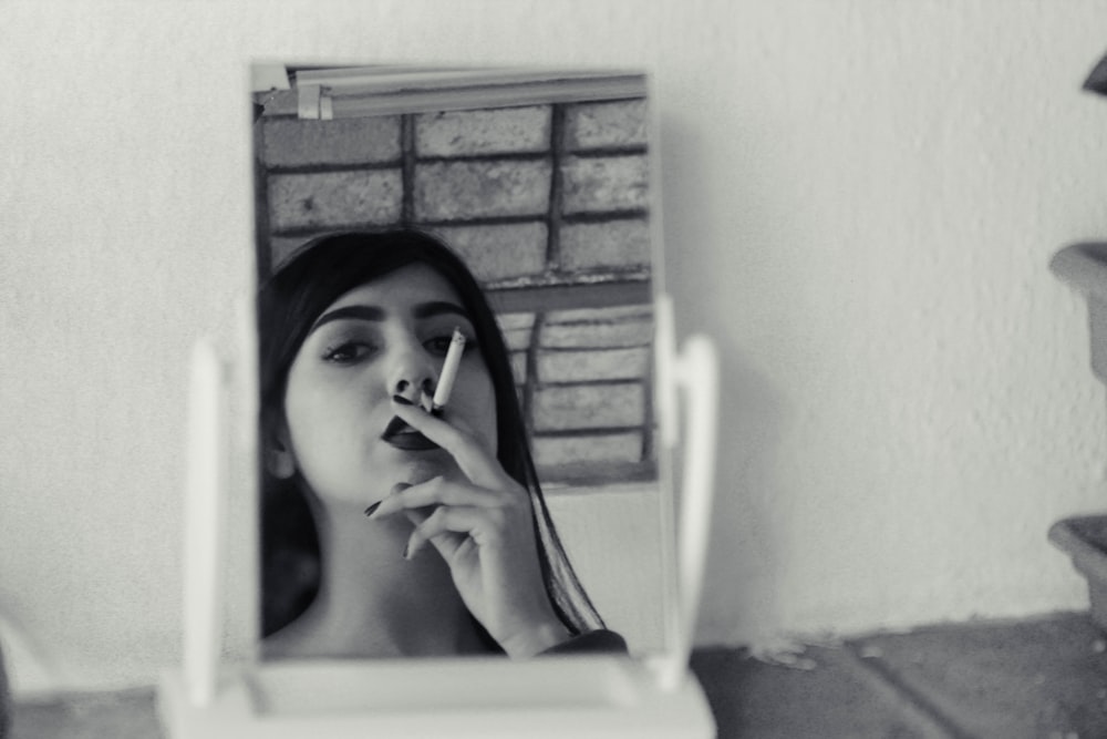 grayscale photo of woman smoking while looking at mirror