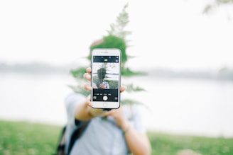 A person looking at their smartphone with a focused expression, surrounded by nature.