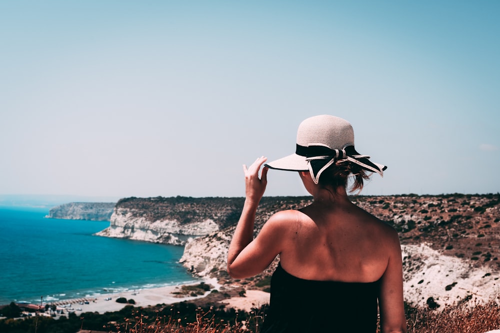 a woman wearing a hat looking at the ocean