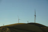 A panoramic view of a wind farm with turbines spinning under a clear blue sky.