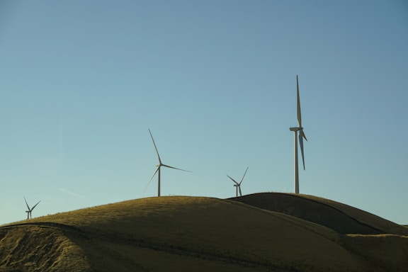 Wind turbines stand tall on rolling hills under a clear blue sky, capturing the serene and vast landscape of a wind farm.