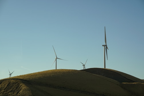 Wind turbines turning gracefully on a breezy hill under a clear blue sky.