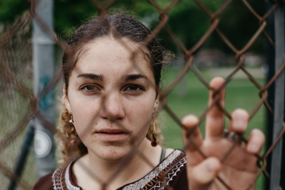 selective focus photography of woman in black top holding on mesh fence