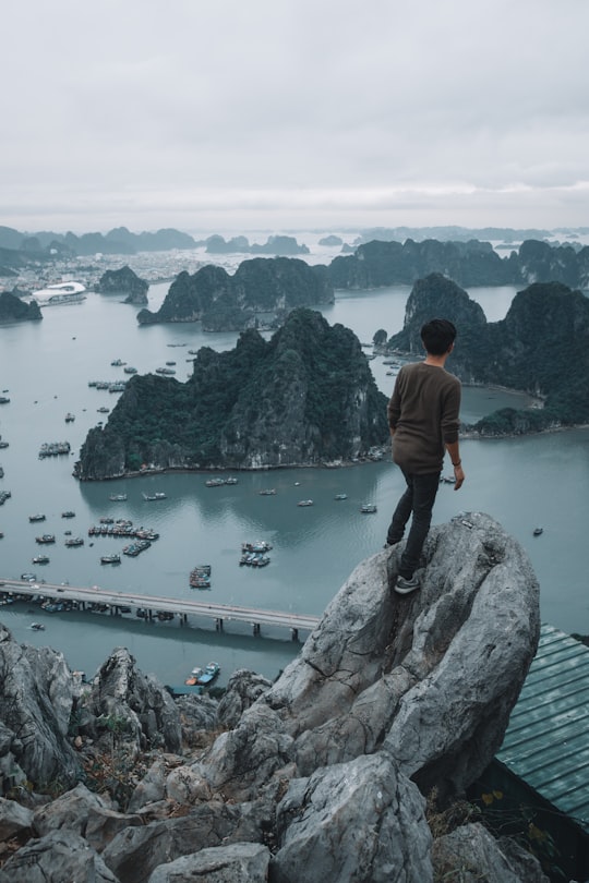man standing on top of a rocky mountain overlooking other islets in Poem Mountain Vietnam