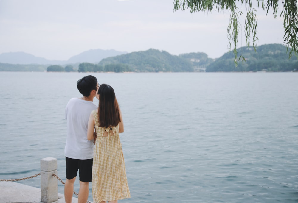 man beside woman in yellow dress beside body of water during daytime