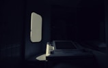 A dimly lit interior with a vintage ATM or ticket machine partially illuminated by light entering through a nearby window. The shadows create a stark contrast between the bright screen and the surrounding darkness.