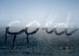 Condensation on a glass surface with the word 'cold' written in it using a finger, allowing clearer sections within the misted area.