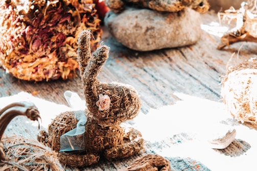 A soft pastel-toned crochet bunny nestled among delicate dried flowers on a wooden table.