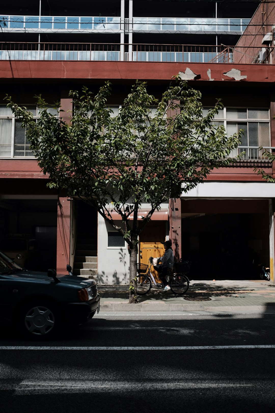 man riding motorcycle parked under tree beside building during daytime